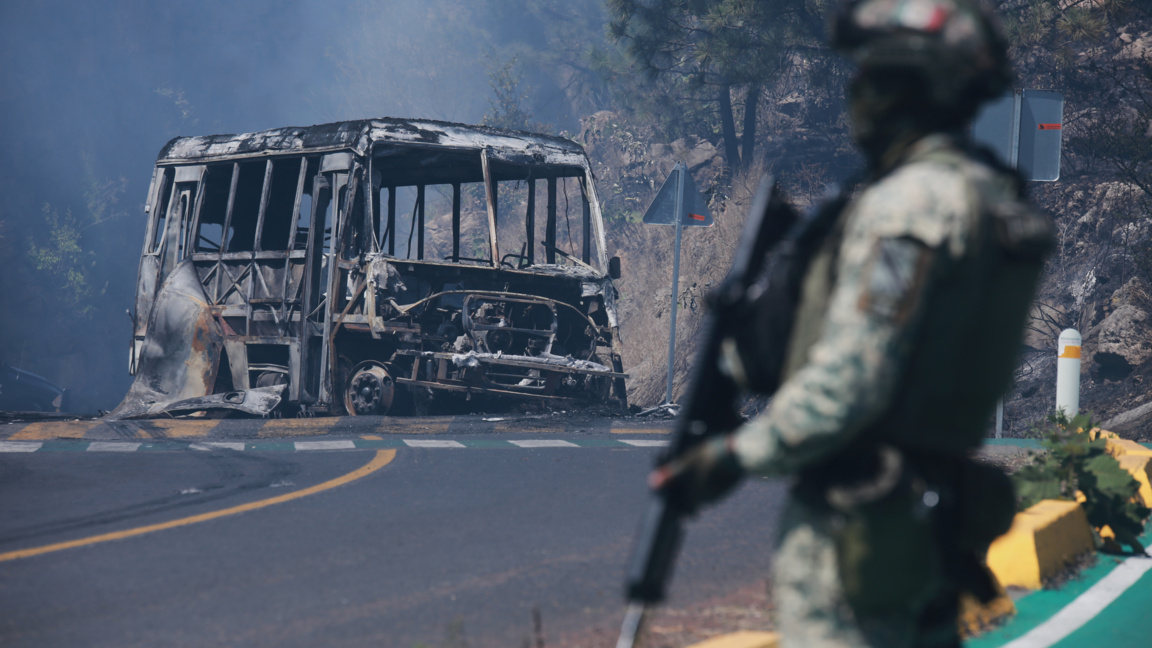 Мексикански войник стои до опожарен автомобил в Коинцио, щата Мичоакан, Мексико, неделя, 22 февруари 2026 г.